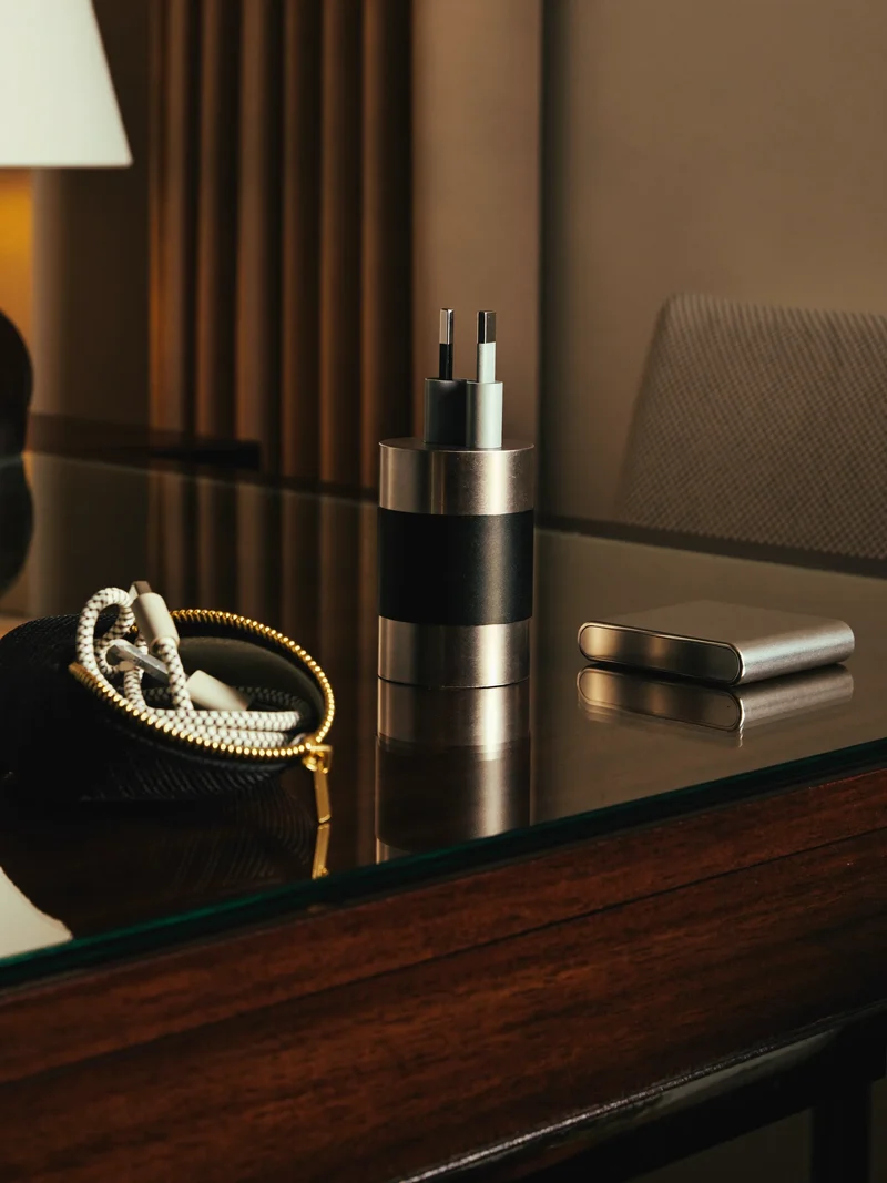 Stikadapter, kabelpose og powerbank på et hotelskrivebord i varmt lampelys